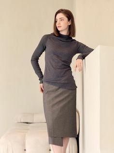 Woman in a dark gray turtleneck and midi skirt leaning against a wall