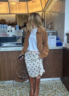 Woman in a brown jacket and polka dot skirt standing in a cafe