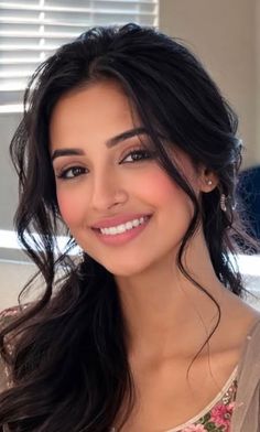 Woman with long dark hair and a nose piercing smiling at the camera