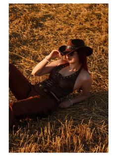 Woman in a cowboy hat and sunglasses lying in a straw field at golden hour
