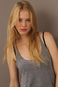 Woman with long blonde hair wearing a gray tank top and black bra strap
