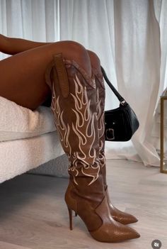 Person wearing brown cowboy boots with white flames and a black handbag