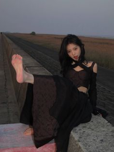 Woman in a black crop top and long skirt posing on a concrete wall at dusk