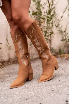 Person wearing brown cowboy boots with white embroidery outdoors