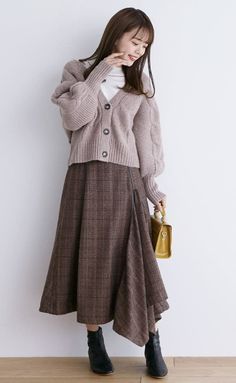 Woman in a brown cardigan and plaid midi skirt holding a small handbag
