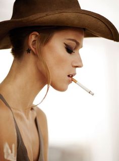 Woman in a cowboy hat with a cigarette in her mouth, profile view