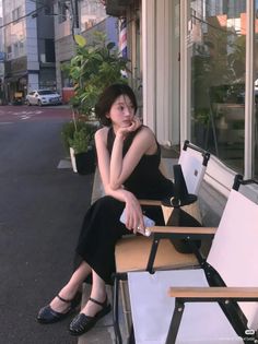 Woman with short hair in a black dress sitting on a chair outdoors