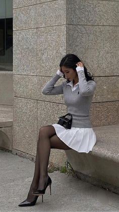 Woman in a gray sweater and white pleated skirt sitting outdoors
