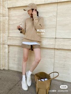 Woman in a cable knit sweater, brown shorts, and a baseball cap outdoors