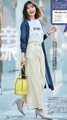 Woman with short hair wearing wide leg pants and a long cardigan, holding a yellow handbag