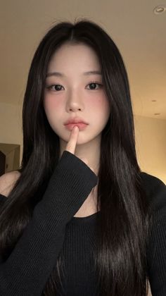 Woman with long black hair and blush makeup, finger on her lips
