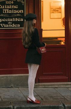 Woman in a beret and white patterned tights standing outside a building