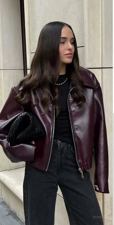 Woman with long dark hair wearing a burgundy leather jacket and black jeans