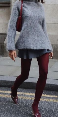Person in a gray sweater, mini skirt, and red tights walking on a street