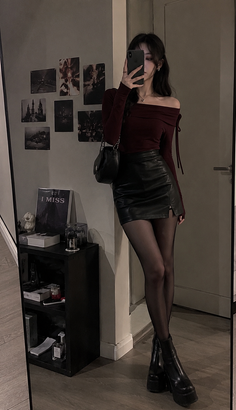 Woman in an off-shoulder top and leather skirt taking a mirror selfie