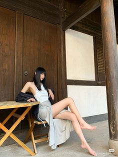 Woman with long black hair sitting barefoot on a wooden chair outdoors