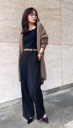 Woman in a brown cardigan and black pants standing outdoors