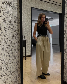 Woman in a black top and wide leg pants taking a mirror selfie