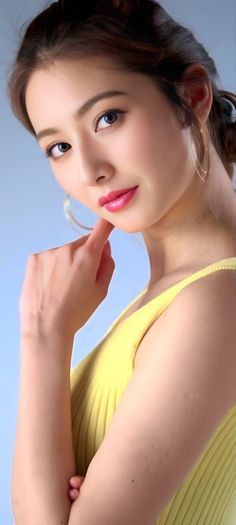 Woman in a yellow top with pink lipstick and hoop earrings against a blue background