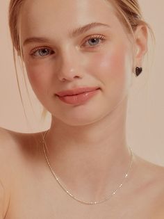 Woman with blonde hair and blue eyes wearing heart earrings and a necklace