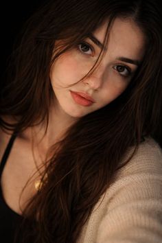 Woman with long brown hair and a gold necklace, wearing a beige cardigan