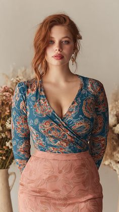 Woman with red hair and blue eyes wearing a patterned top and pink skirt