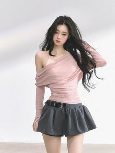 Woman with long black hair wearing a pink top and mini skirt against a white background