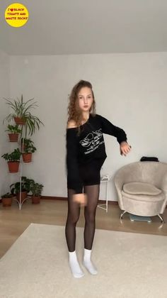 Woman in a black sweatshirt, black tights, and white socks indoors