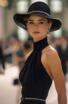 Woman in a black hat and dress with earrings, looking directly at the viewer