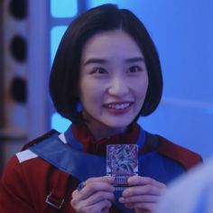 Woman with short hair in a red and blue jacket holding a card