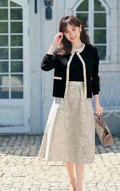 Woman in a black cardigan and floral skirt holding a handbag outdoors