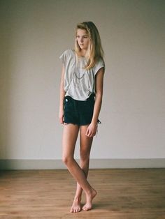Young woman with blonde hair and denim shorts standing barefoot indoors