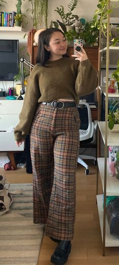 Woman in a chunky sweater and plaid pants taking a mirror selfie indoors