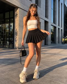 Woman in a black pleated skirt and white crop top outdoors during golden hour