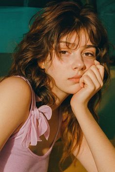 Young woman with long wavy hair in a pink top, resting her chin on her hand