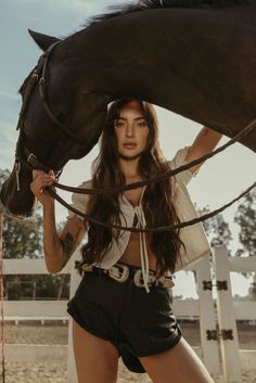 Woman in a crop top and leather shorts with a horse at a ranch