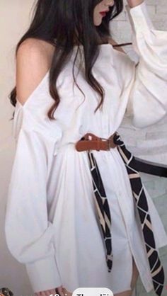 Woman with long dark hair wearing a white off-shoulder dress with a belt and scarf