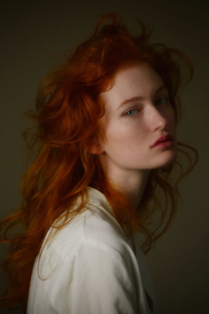 Woman with long red hair and blue eyes wearing a white shirt