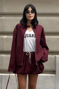 Woman with black hair and sunglasses wearing a maroon jacket and shorts