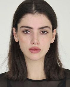 Woman with dark hair and freckles wearing a sheer top, looking directly at the camera
