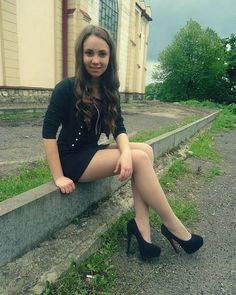 Woman in a black dress and high heels sitting on a curb outdoors