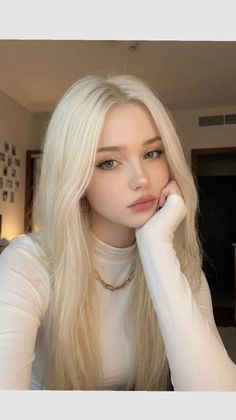 Woman with long blonde hair wearing a white turtleneck and gold chain necklace