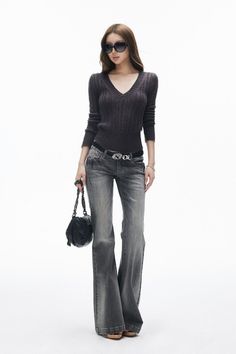 Woman with long hair wearing sunglasses, a v-neck sweater, and flared jeans