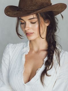 Woman in a cowboy hat and white shirt with braided hair looking down