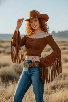 Woman with red curly hair wearing a cowboy hat and fringe top in a desert landscape