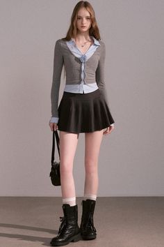 Woman in a pleated skirt, cardigan, and combat boots standing indoors
