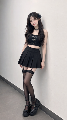 Woman in a black crop top, pleated skirt, and thigh-high stockings leaning against a wall