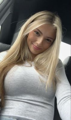 Blonde woman with long hair wearing a white top, smiling indoors