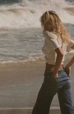 Blonde woman with long hair standing on a beach with ocean waves in the background