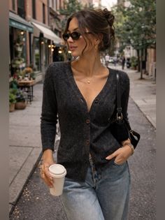 Woman in a dark cardigan and jeans walking on a street with a coffee cup